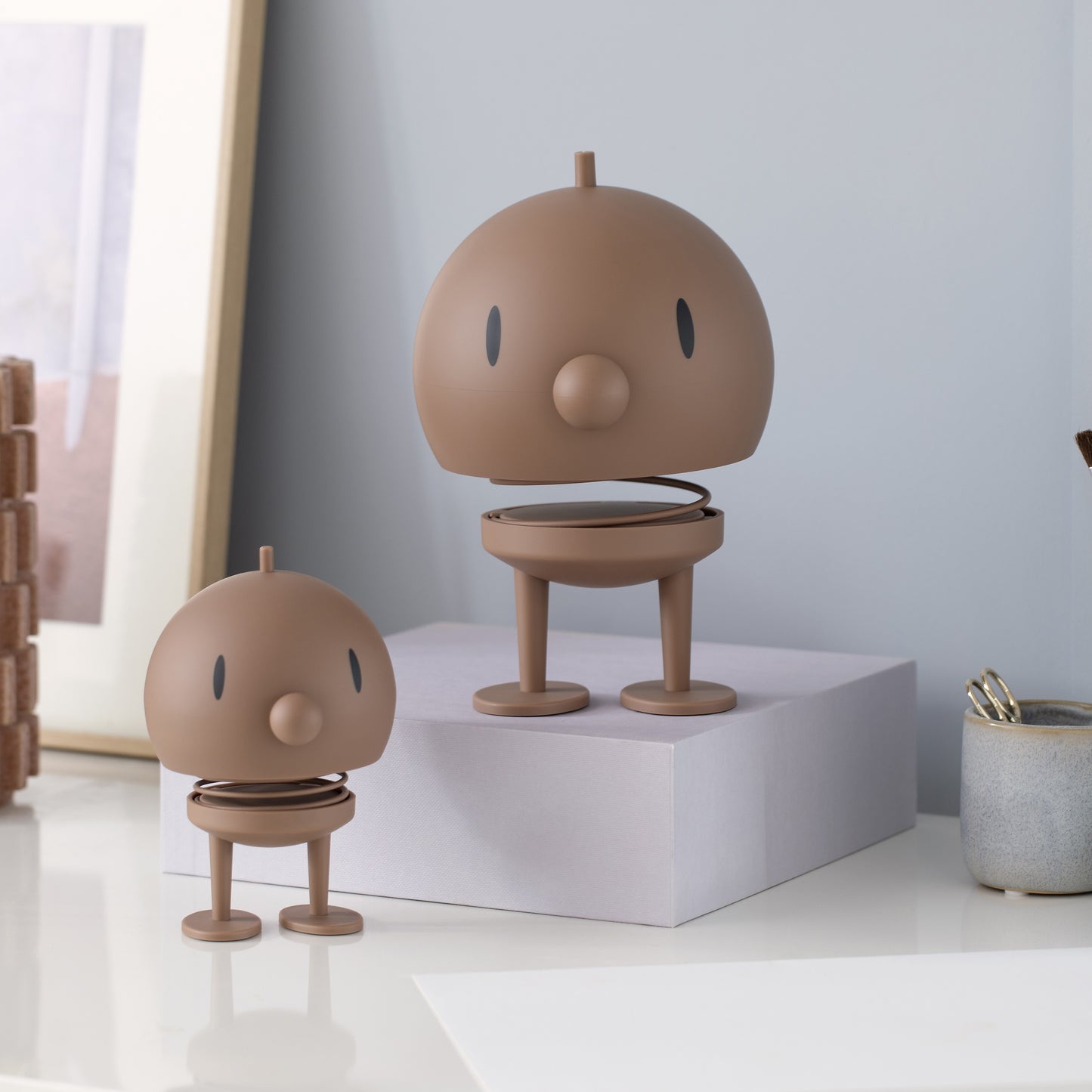 Two brown cartoon-like figurines on a white surface with a light gray wall in the background.