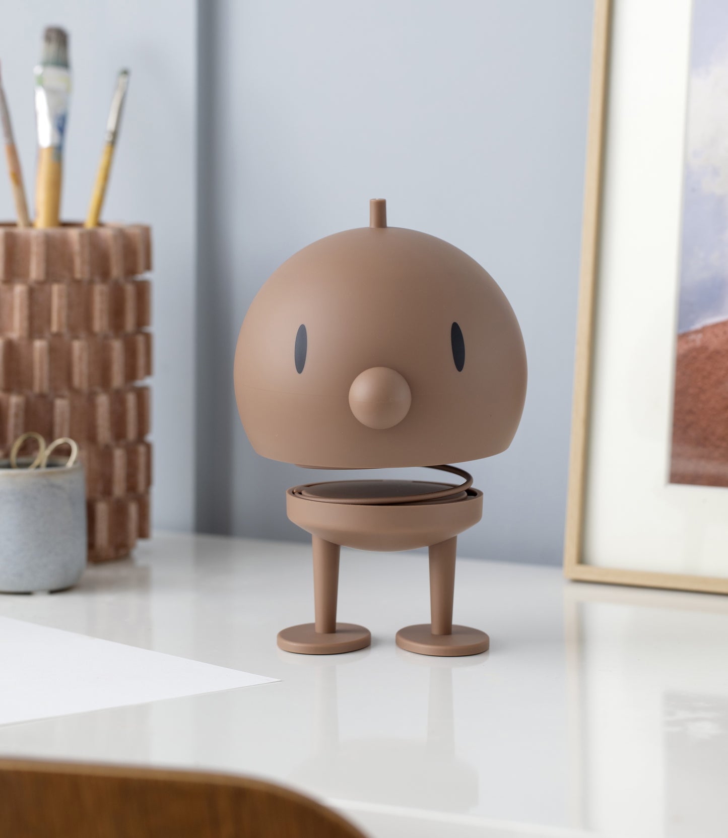Brown robot-like figurine on a desk with a neutral background