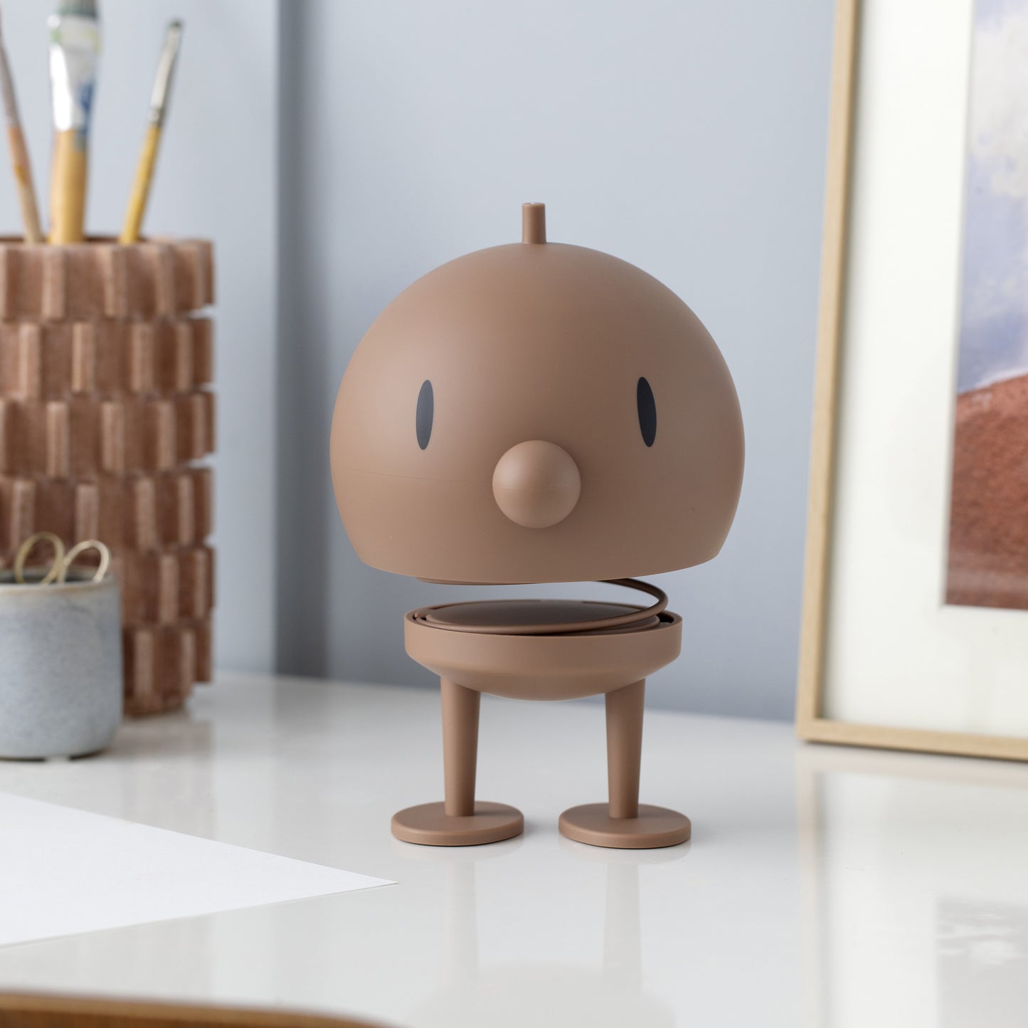 Brown robot-like figurine on a desk with a neutral background